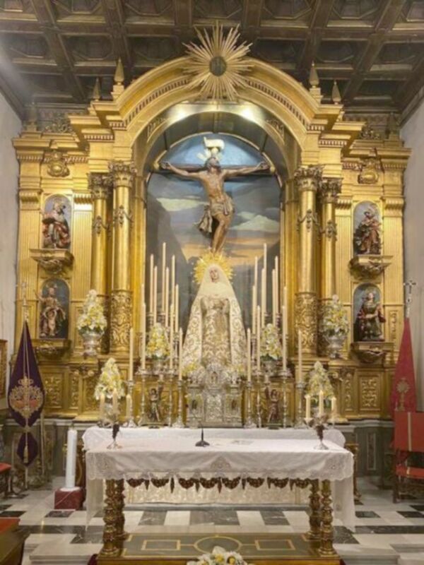 Imagen de una iglesia con un altar dorado y dorado, en el centro hay una imagen de Cristo crucificado. En la parte superior del altar se encuentra una imagen de la Virgen María, rodeada por varios santos y ángeles. La iglesia tiene una decoración barroca con detalles dorados y dorados, y el techo es de madera.