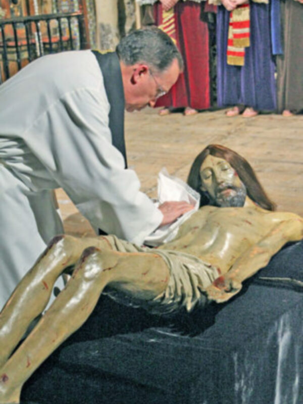 Un sacerdote bendice el cuerpo de un Cristo crucificado en una iglesia, rodeado por personas vestidas con trajes tradicionales.
