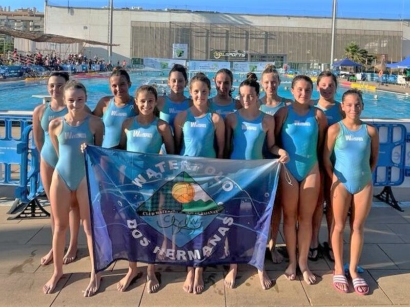 Equipo de natación femenina posando con la bandera de su club en una piscina de competición.
