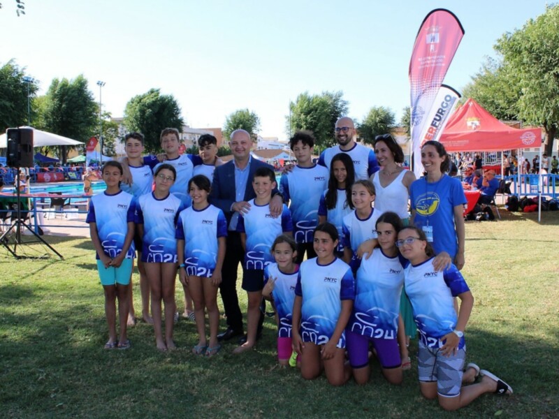 Equipo de natación PNYC posando para una foto en un evento deportivo al aire libre.