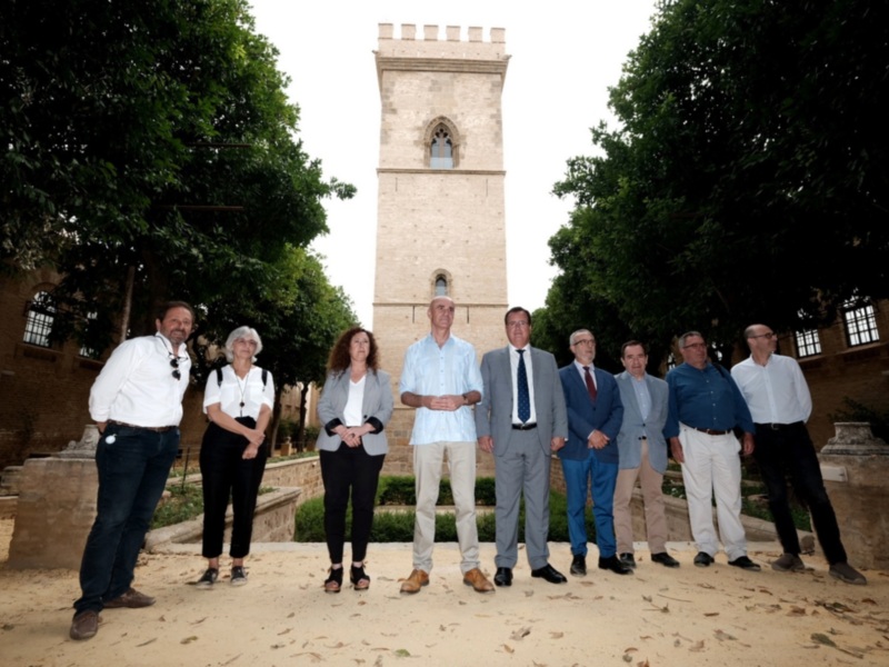 Fotografía de una reunión formal en un entorno histórico con personas vestidas de negocios y una torre medieval al fondo.