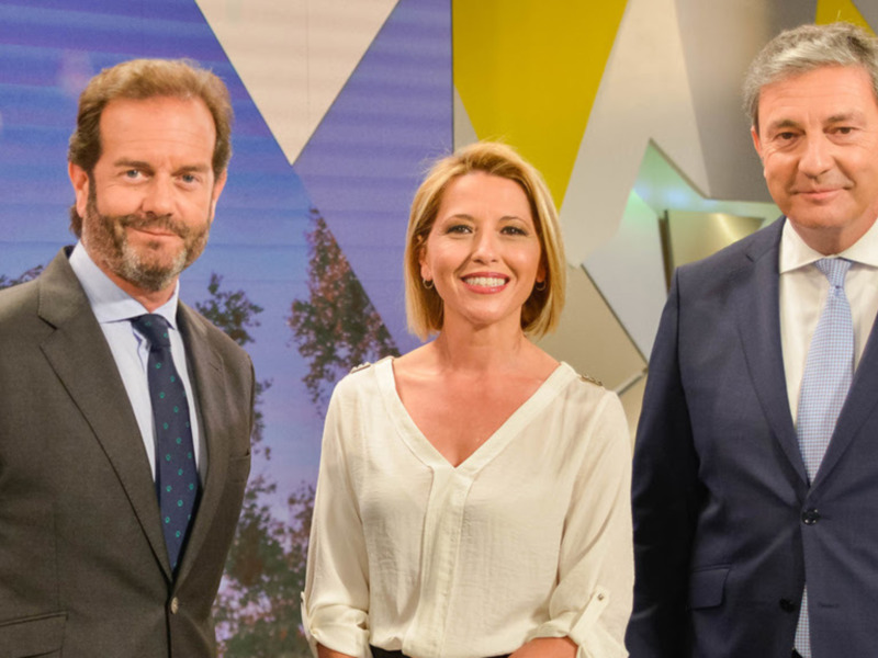 Tres personas en trajes posando frente a un fondo con formas geométricas en azul, blanco y amarillo.