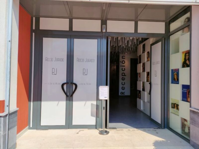 Puerta de entrada a un edificio con dos puertas grandes y una recepción visible a través de una ventana.