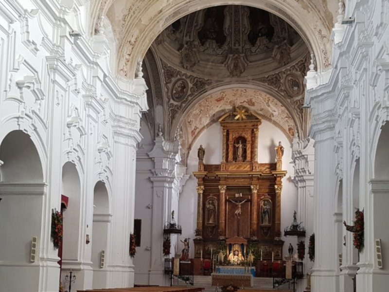 Interior de una iglesia con arcos y columnas blancas, altar dorado en el fondo.