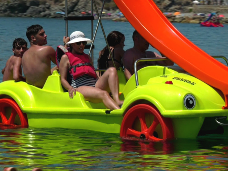 Gente disfrutando de un día soleado en un barco pedaleable en el mar.