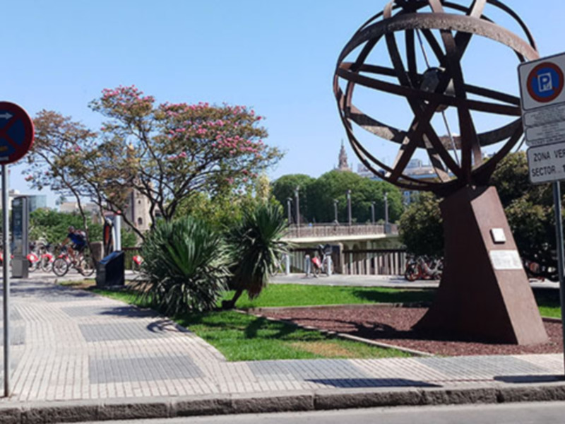 Escultura en el parque con árboles y una señal de tráfico en el fondo.