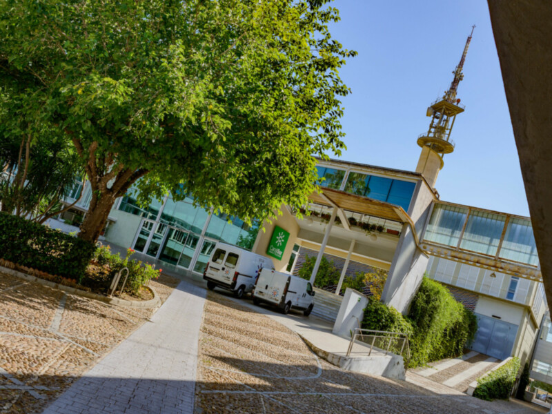 Edificio moderno con torre de telecomunicaciones, jardín y camiones de servicio en el patio.