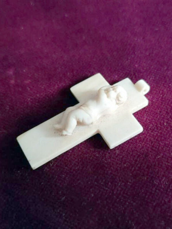 Miniatura de cruz con figura de niño en una superficie purpura