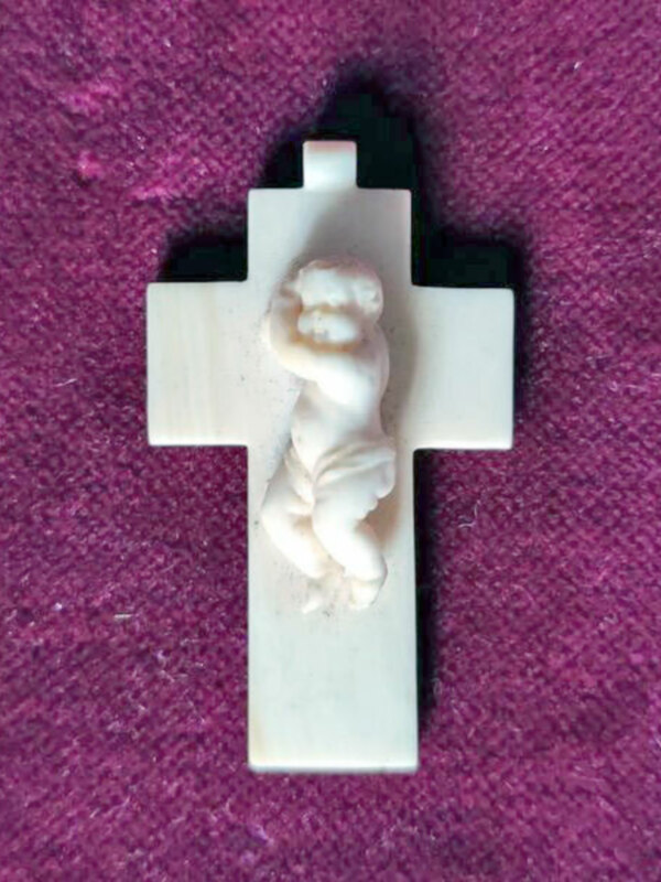 Crucifijo de hueso con figura de Jesús, colocado sobre fondo de color morado.