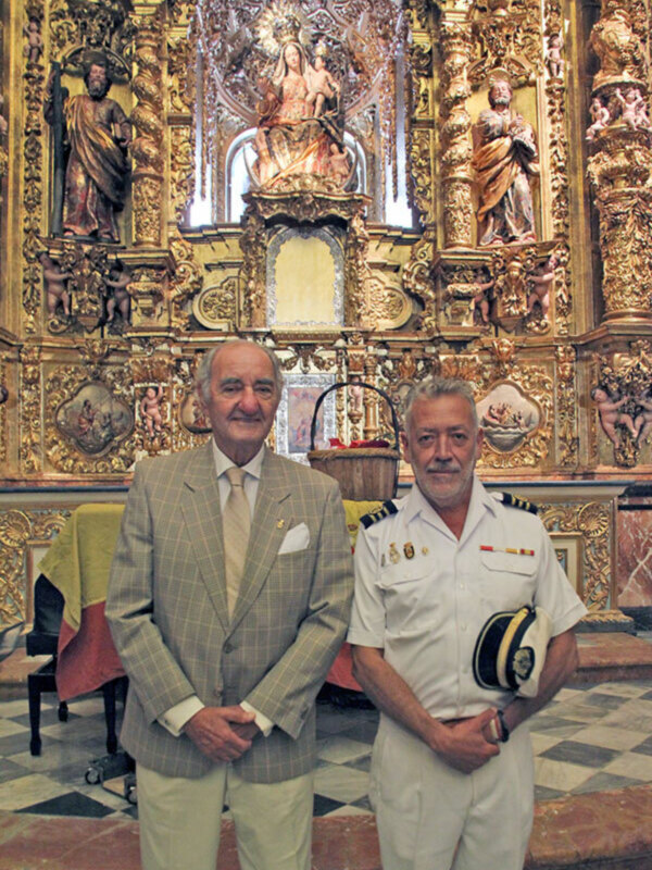 Dos hombres posan frente a un altar dorado con esculturas y una imagen central.
