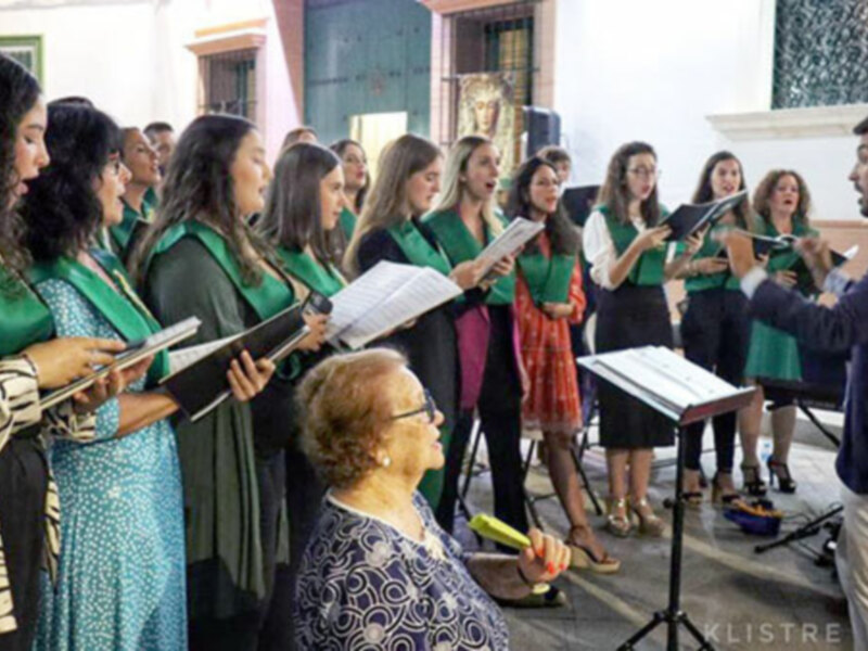 Concierto coral en una iglesia, dirigido por un hombre y con una audiencia atenta.
