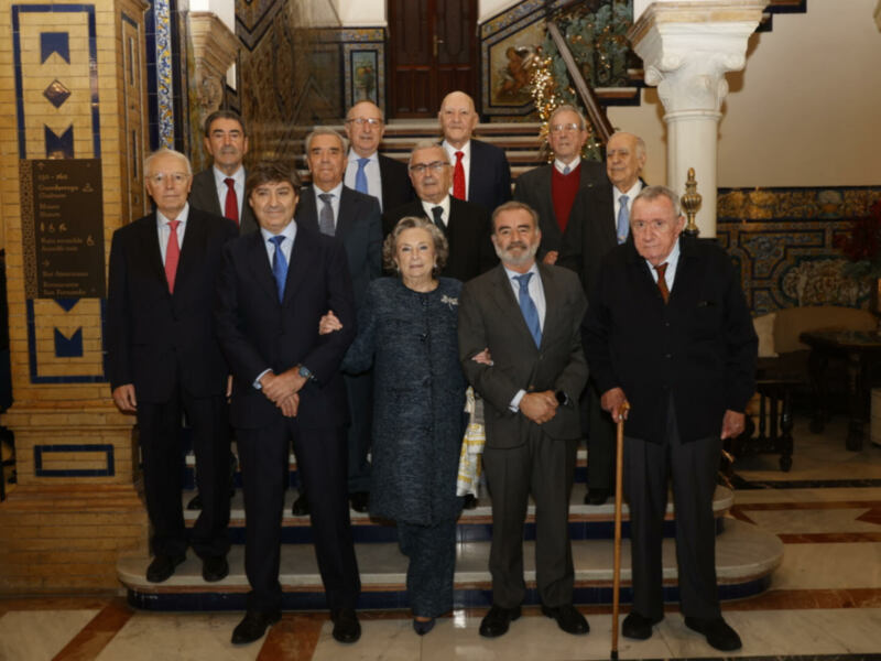 Grupo de personas posando en un entorno elegante con azulejos y decoración clásica. La imagen muestra a varias personas vestidas con trajes formales, posando para una foto en una escalera con azulejos y una decoración clásica en el fondo.