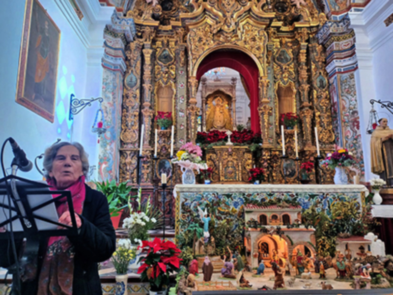 Una mujer en una iglesia, frente al altar dorado con figuras religiosas y flores, posiblemente durante una ceremonia religiosa.