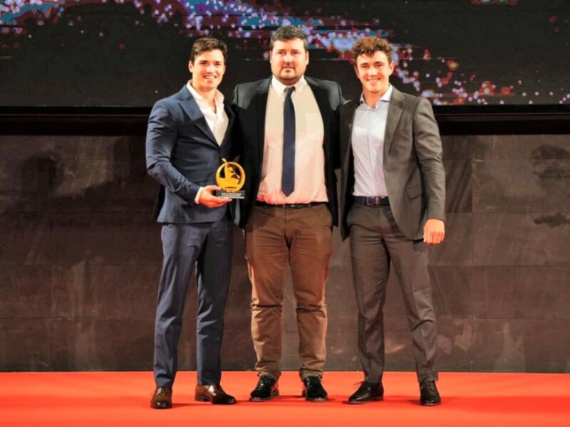 Tres hombres en trajes celebran un premio en una ceremonia formal.