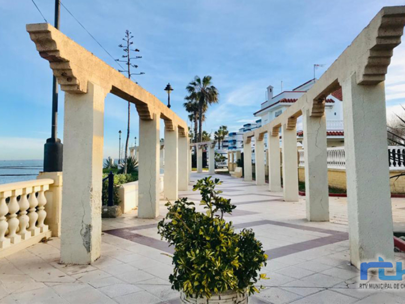 Arco de piedra en un parque con palmeras y mar al fondo.