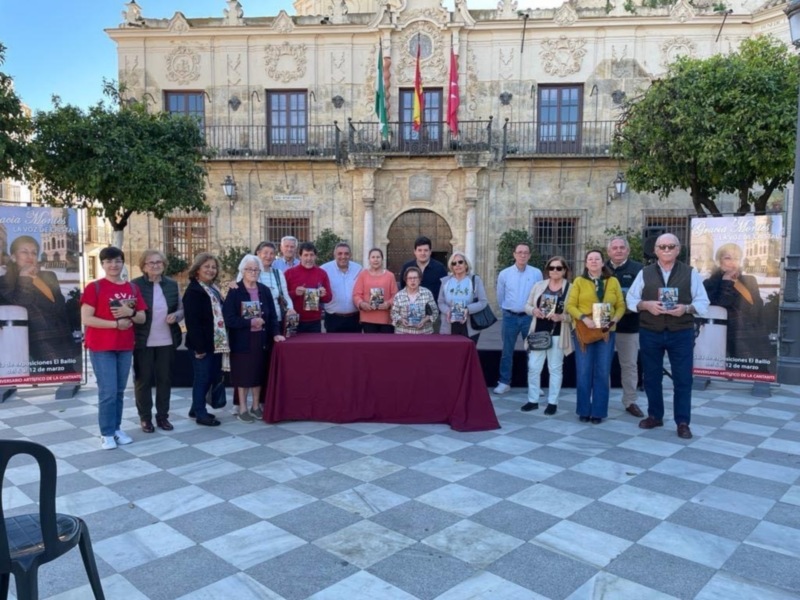 Gruppo di persone posa per una foto davanti a un palazzo storico con bandiere spagnole.