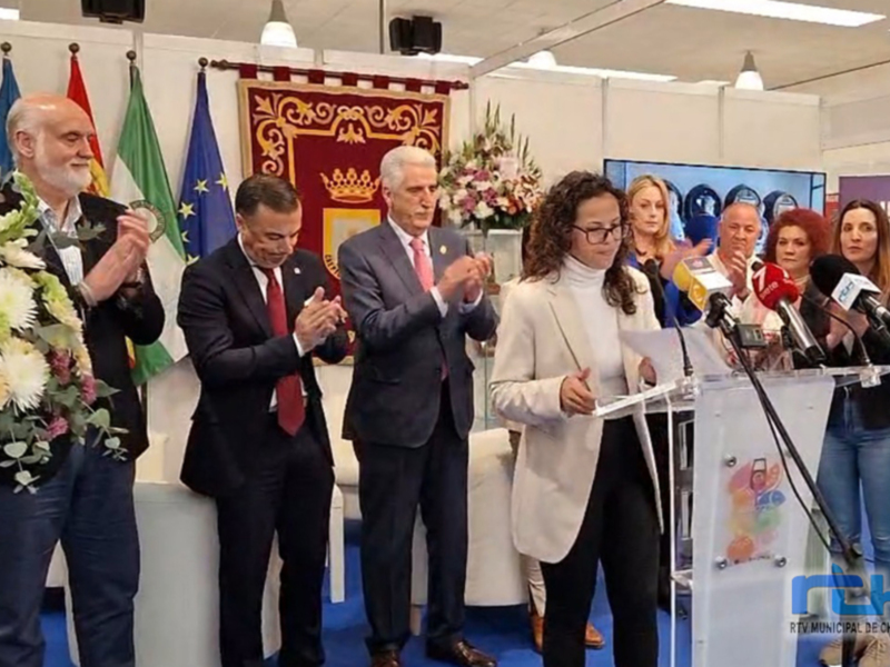 Una conferencia de prensa en un evento oficial, con personas en trajes y micros de prensa, en un entorno con banderas y flores. El texto en la pantalla dice 'RTV MUNICIPAL DE CHIPONA'.