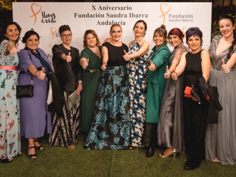 Celebración del X Aniversario de la Fundación Sandra Ibarra en Andalucía. Una foto de grupo con varias personas posando juntas, todas vestidas formalmente y sonriendo. El fondo muestra un cartel con el nombre de la fundación y su logotipo.
