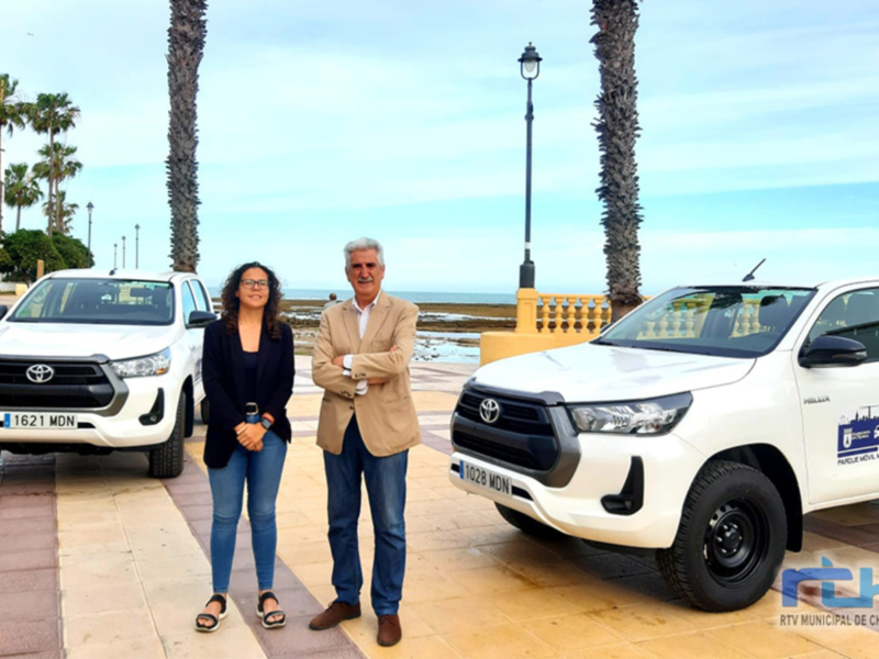 Dos personas posan junto a un Toyota Hilux blanco en una acera con palmeras y el mar al fondo. La imagen promociona un evento de la Municipalidad de Chipiona, con el logo y nombre visible en el fondo.