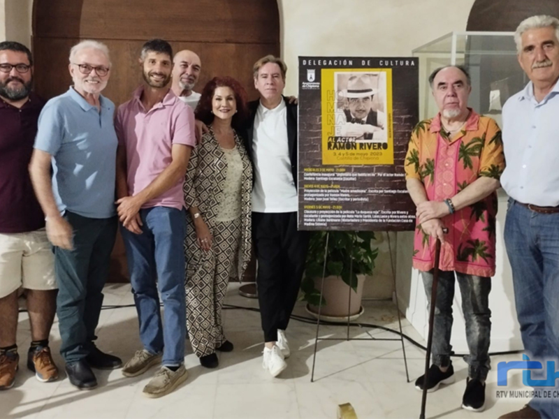 Grupo de personas posando frente a una cartelera con información sobre la Delegación de Cultura.