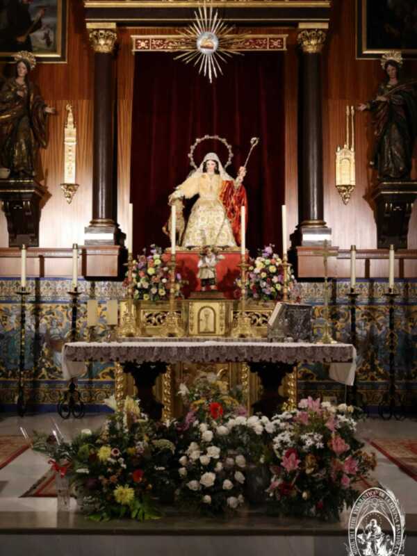 Imagen de una iglesia con un altar dorado, estatuas religiosas y flores.