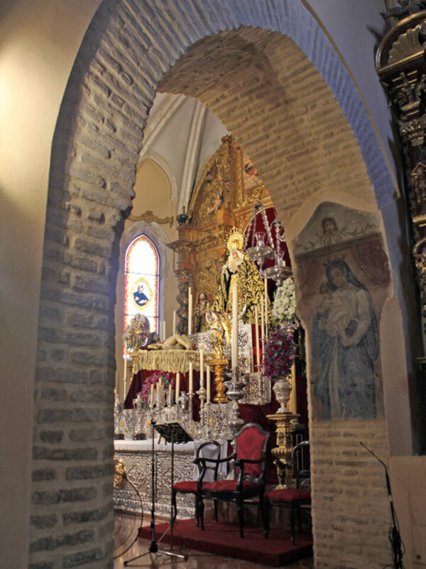 Interior de una iglesia con arcos y vitrales, mostrando un altar con estatuas religiosas.