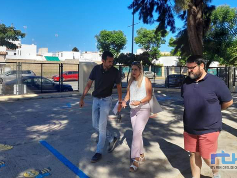 Tres personas caminando por una calle con árboles y coches al fondo, bajo un cielo azul claro.