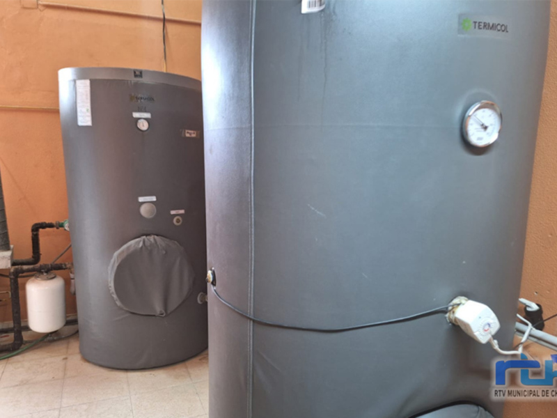 Un sistema de calefacción con un calentador de agua Termicol, junto a un tubo de ventilación y un tanque de agua. El calentador es de color gris y está conectado a un cable.