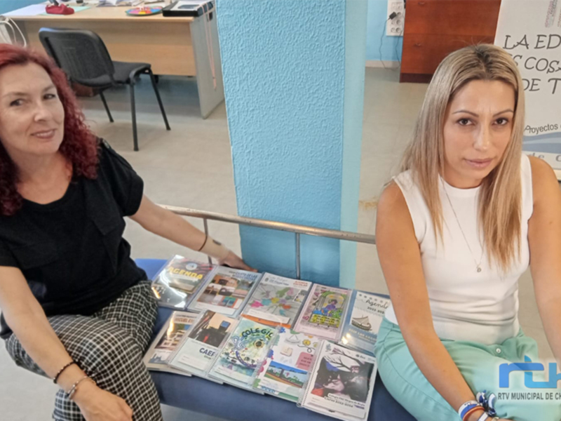 Dos personas sentadas en un banco, con libros y revistas al frente. Contexto: escuela o biblioteca.