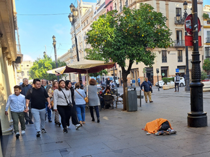Paseo por la ciudad con gente caminando y una persona sin hogar acostada en el suelo.