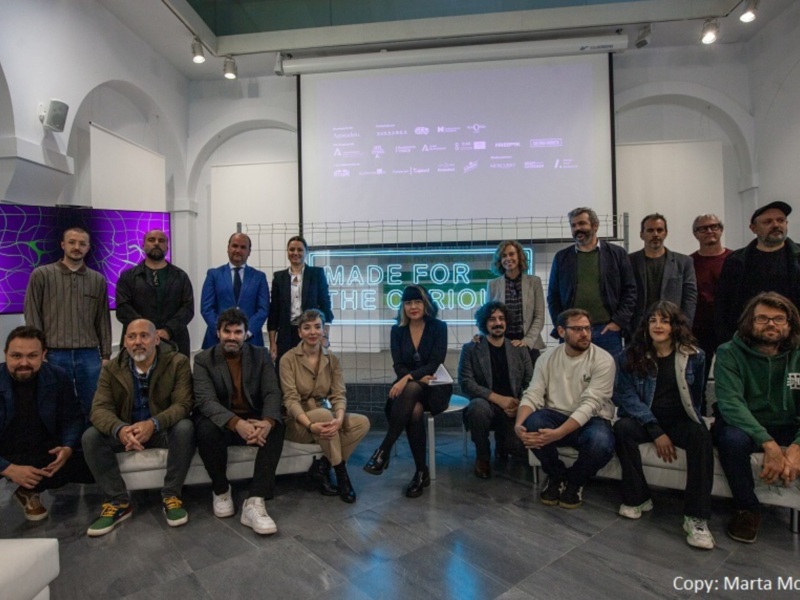 Grupos de personas sentadas en una sala con un fondo de proyección que muestra "Made for the curious". El ambiente es informal y creativo.