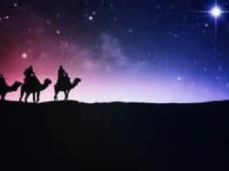 Tres reyes magos en camello recorren el desierto bajo un cielo estrellado y una brillante estrella.