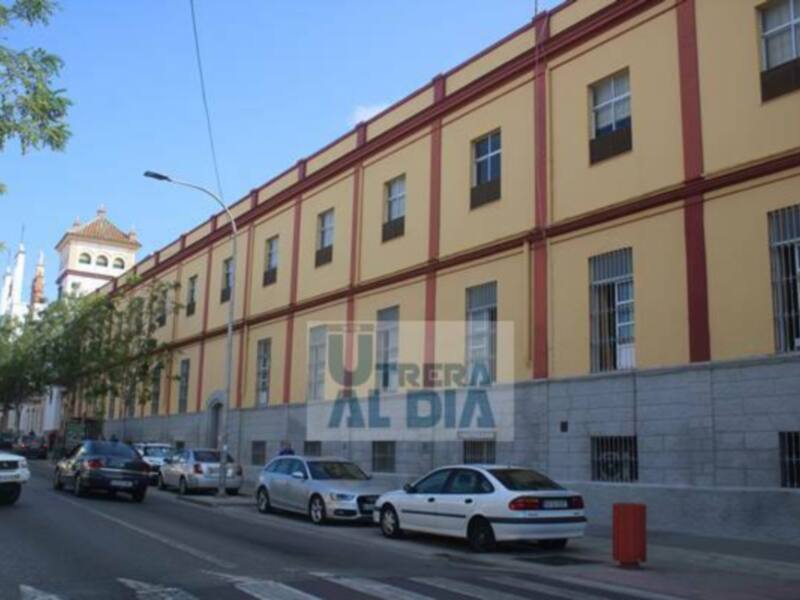 Fachada de un edificio con detalles arquitectónicos, incluyendo ventanas y balcones, con coches estacionados en la calle y árboles al lado.