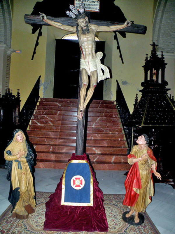 Crucifijo en iglesia con estatuas de personas a ambos lados.