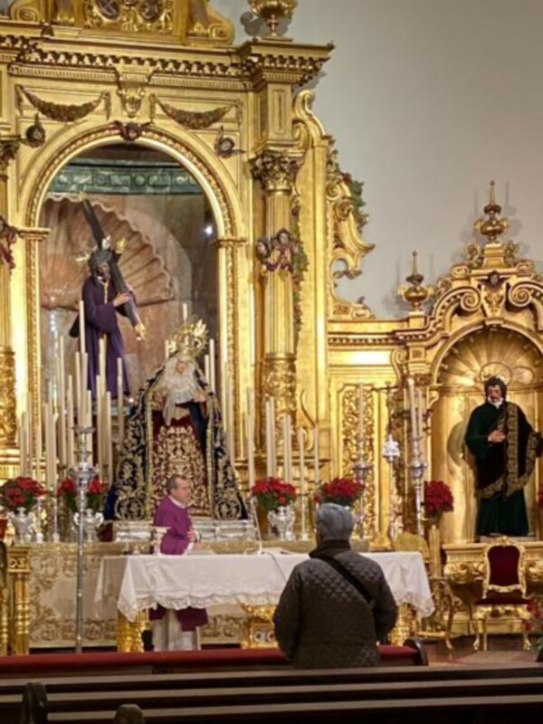 Interior de una iglesia con altar dorado y estatua religiosa. Personas rezando en el fondo.
