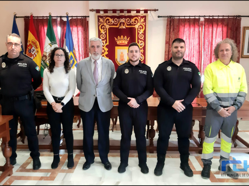 A una persona en uniforme de policía junto a otros individuos, posiblemente autoridades o funcionarios. La escena se desarrolla en un entorno formal, con banderas y decoración institucional. La imagen parece estar relacionada con una reunión o conferencia de trabajo en un entorno oficial.