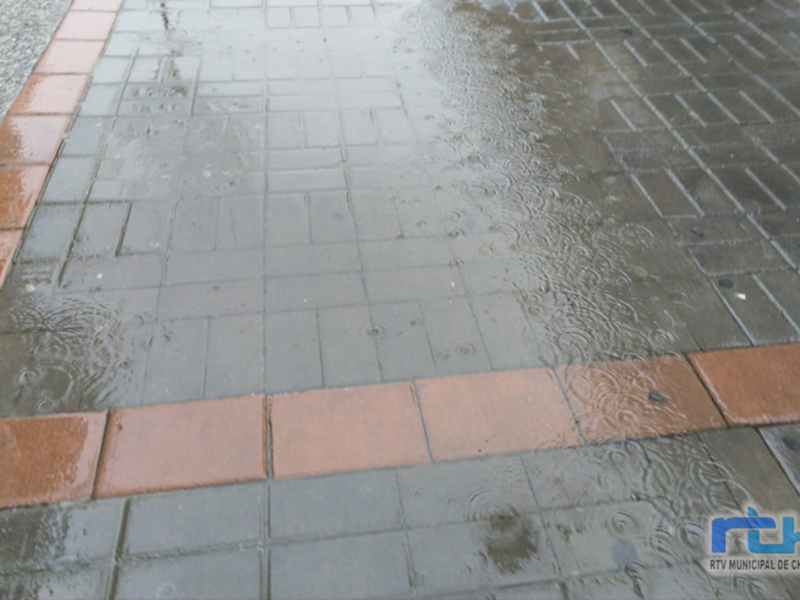 Un camino de adoquines con un patrón de cuadros en tonos grises y rojos, cubierto por una capa de agua después de la lluvia.