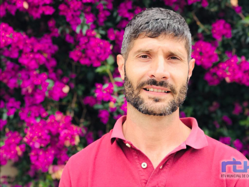 Retrato de hombre sonriente frente a flores de buganvilla violeta.