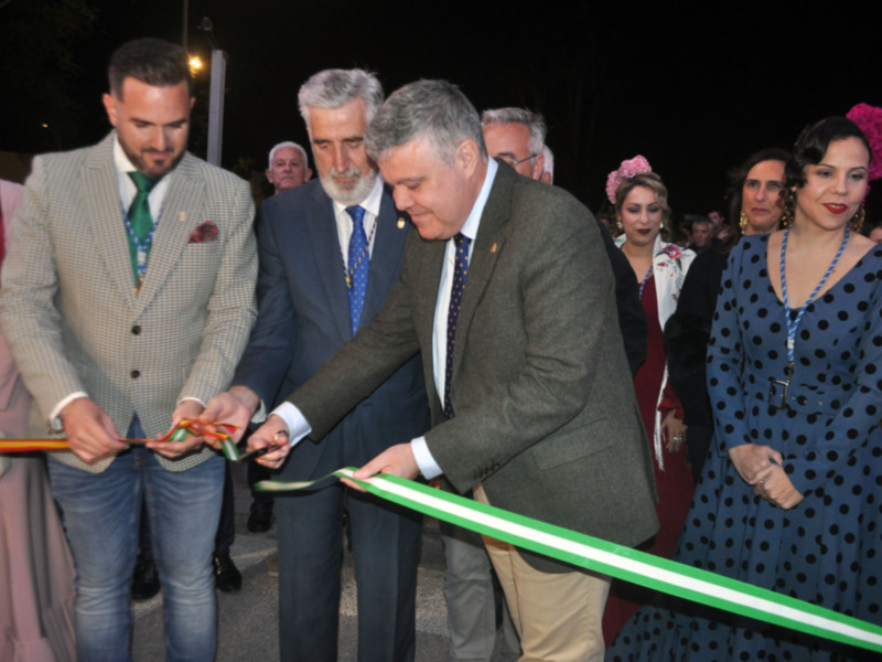 Inauguración de una obra pública en un evento festivo, con personas en trajes formales y una mujer en traje de flamenca.