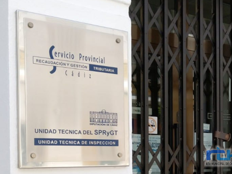 Placa de la Unidad Técnica de Inspección del Servicio Provincial de Recaudación y Gestión Tributaria de Cádiz, ubicada en una puerta de metal con rejas. La placa contiene información sobre la entidad y su ubicación en la ciudad de Cádiz.