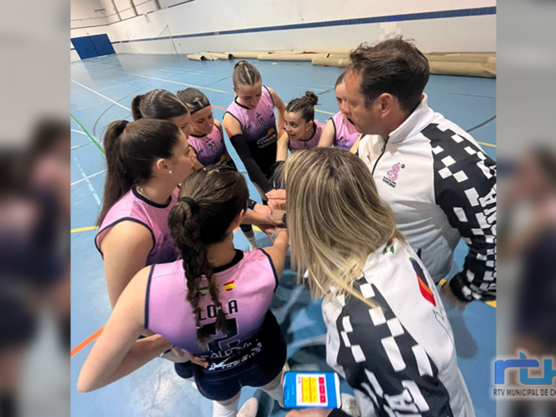 Equipo femenino de baloncesto en un entrenamiento, con una mujer en el centro del círculo y otros miembros de la escuadrilla alrededor. La imagen muestra una cancha de baloncesto con líneas y bordes, y a la derecha se puede ver el logo de RTV Municipal de Chipiona.