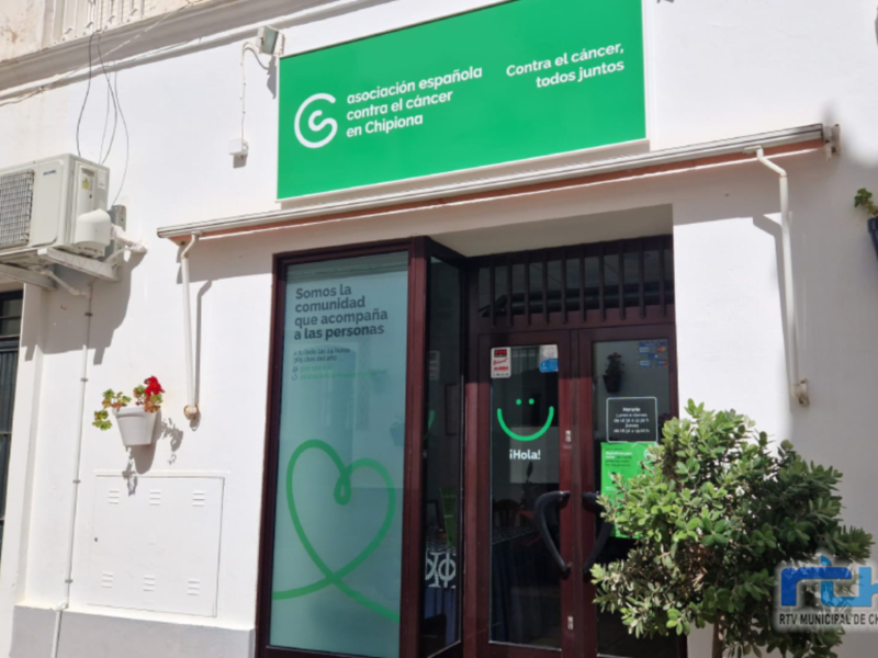 Entrada de la Asociación Española Contra el Cáncer en Chipiona, con letrero verde y mensaje de apoyo a las personas con cáncer.