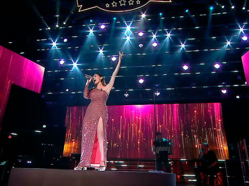 Una cantante en un escenario brillante, con luces y telón de fondo rojo.