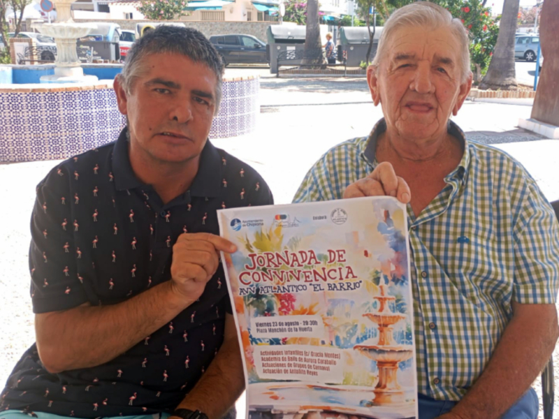 Dos personas sosteniendo un cartel informativo sobre una jornada de convivencia en la playa 'El Barrón'.