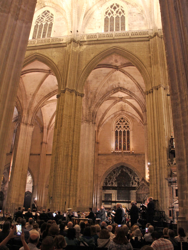 Interior de una catedral con arcos y columnas, donde una orquesta está tocando.