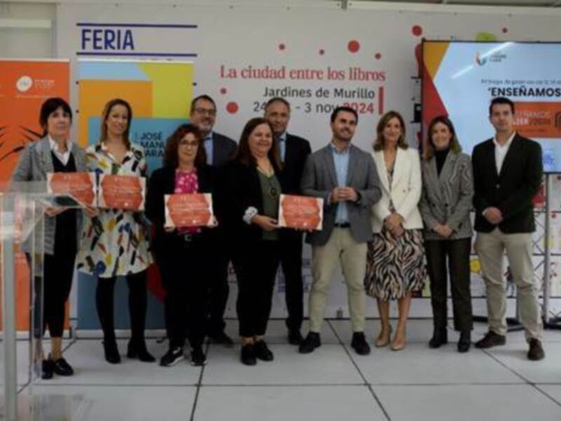 Una foto de grupo de personas en una feria, con carteles y un fondo de pared con información sobre la feria.