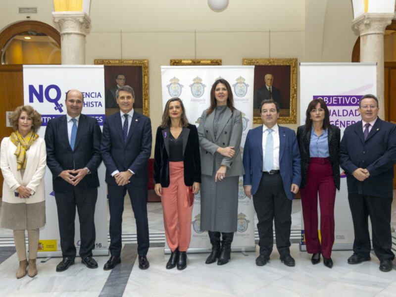Grupo de personas posando frente a un fondo con banderas y carteles de la Asociación de Abogados de España. El objetivo es promover la igualdad de género en la abogacía.