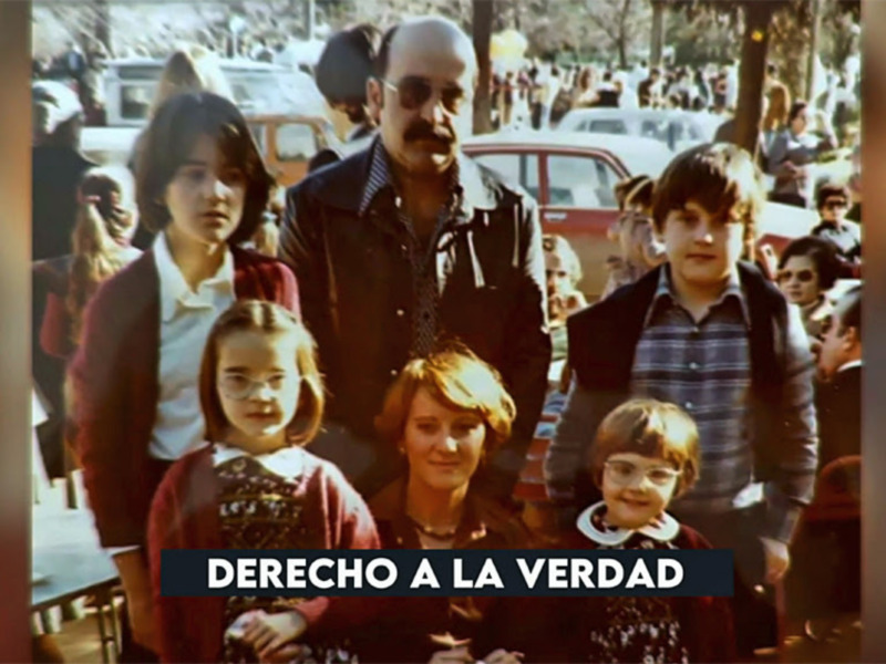 Una familia en un evento público, con personas y vehículos en el fondo.