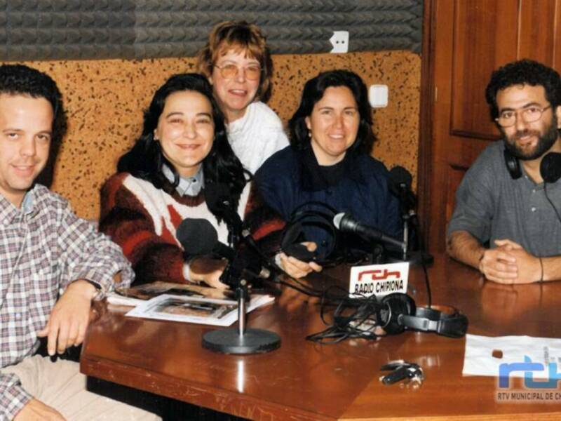 Grupo de personas en un estudio de radio, sosteniendo micrófonos y con material de producción en la mesa. El ambiente es profesional y se puede ver un logo de la emisora en el fondo.