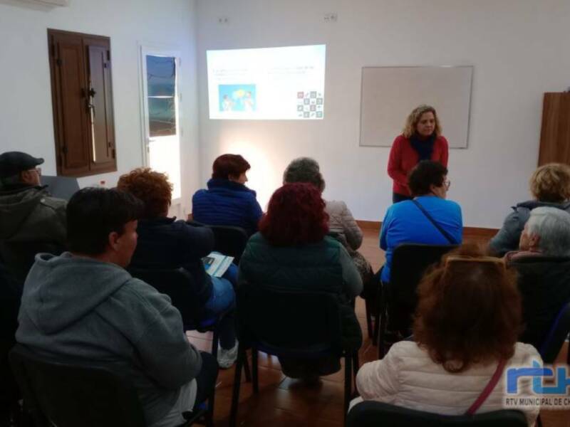 Una mujer en rojo presenta una diapositiva en una sala de conferencias, mientras un grupo de personas la observan atentamente.